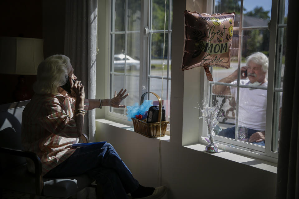 FILE - In this Sunday, May 10, 2020 file photo, Mary Faye Cochran, 86, sings "You Are My Sunshine" over the phone to her son Stacey Smith through a window for a Mother's Day celebration at Provident Village at Creekside assisted living facility in Smyrna, Ga. The U.S. has been dramatically disrupted in a matter of months, brought low by a global pandemic, Depression-era economic dislocation, and then, nationwide unrest over racial injustice. (AP Photo/Brynn Anderson)