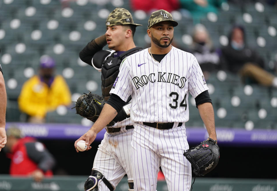 As Colorado Rockies catcher Dom Nunez, back, heads behind the plate, relief pitcher Jordan Sheffield (34) takes a new ball after throwing a wild pitch to allow the go-ahead run to score from third base for the Cincinnati Reds in the ninth inning of a baseball game Sunday, May 16, 2021, in Denver. (AP Photo/David Zalubowski)