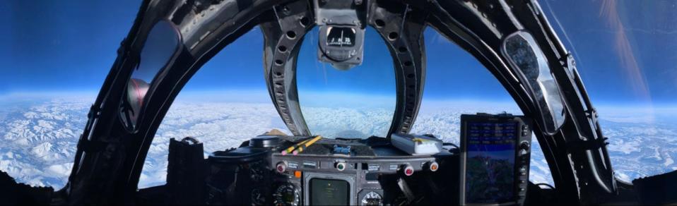 A picture from inside a cockpit shows the sky and clouds below