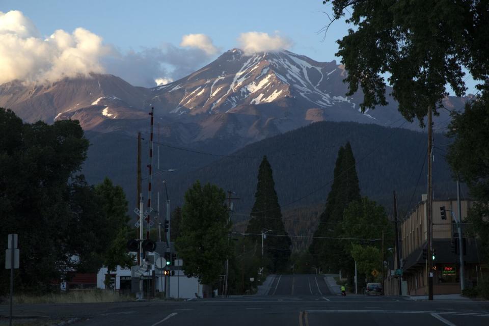 Mountain peaks streaked with snow and topped with clouds rise behind a small-town railroad crossing