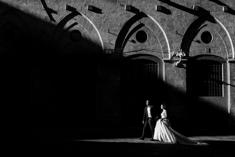 A black and white photo of a bride and groom walking outside of a church.
