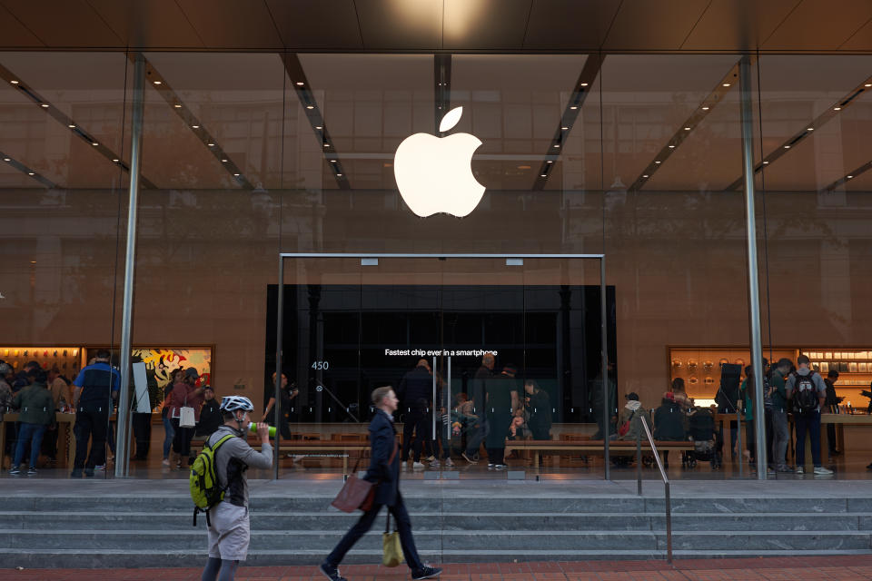 Portland, Oregon, USA - Oct 1, 2019: A man strides past an Apple Store in downtown Portland. The big screen inside is seen advertising Apple's fastest A13 Bionic chips in the new iPhone series.