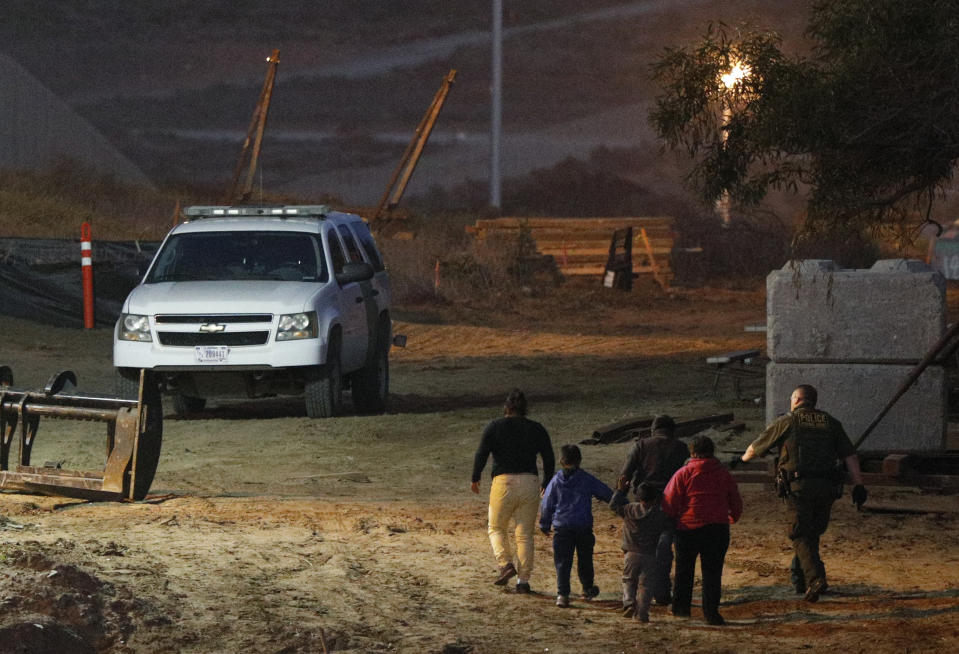 FILE - In this Dec. 3, 2018, file photo, migrants are escorted by a U.S. Border Patrol agent as they are detained after climbing over the border wall from Playas de Tijuana, Mexico, to San Ysidro, Calif. The Trump administration expects to launch a policy as early as Friday, Jan. 25, that forces people seeking asylum to wait in Mexico while their cases wind through U.S. courts, an official said, marking one of the most significant changes to the immigration system of Donald Trump's presidency. (AP Photo/Rebecca Blackwell, File)