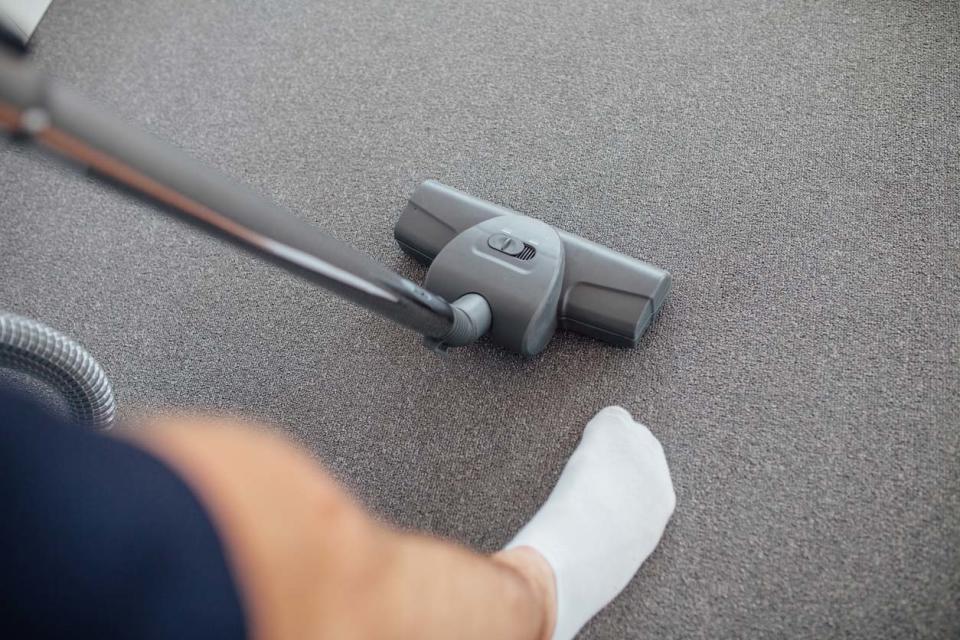 A person in white socks and shorts pushes a vacuum across a grey carpet.