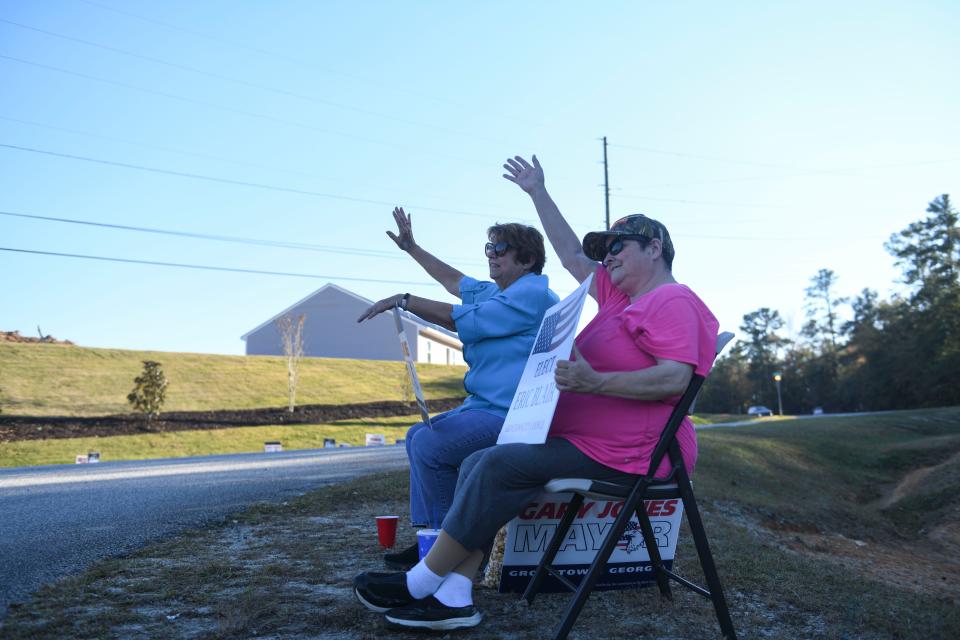 Terry Hays (left) and Tammy Cochrane (right) wave to passing cars outside the entrance to Liberty Park in Grovetown, Ga., on Tuesday, Nov. 7, 2023.