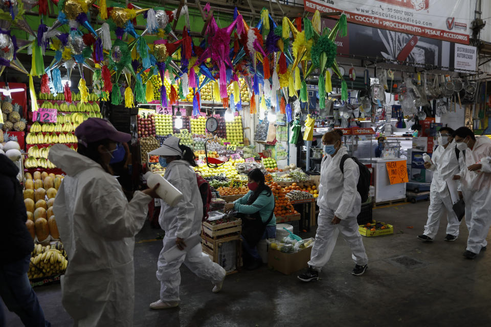 Workers wearing protective suits walk to take up positions to dispense antibacterial gel to passing shoppers and workers, inside the Central de Abastos, the capital's main market, in Mexico City, Tuesday, Dec. 8, 2020.(AP Photo/Rebecca Blackwell)