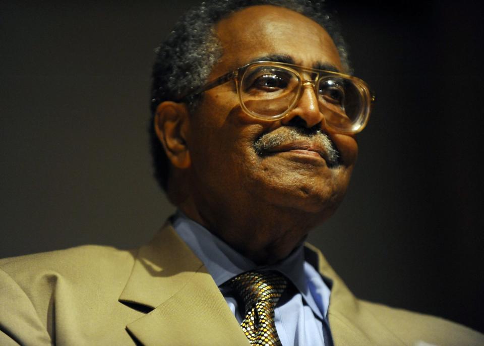 franklin mccain, wearing a tan suit and gold tie and orange rimmed glasses, looks off camera