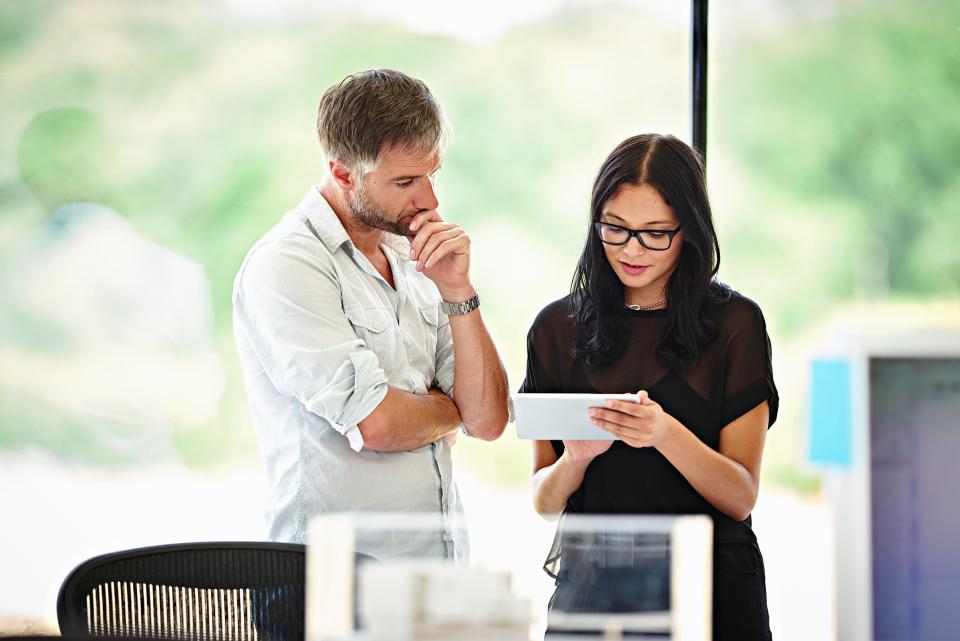 Latina woman and white, male co-worker in discussion while looking at a tablet.