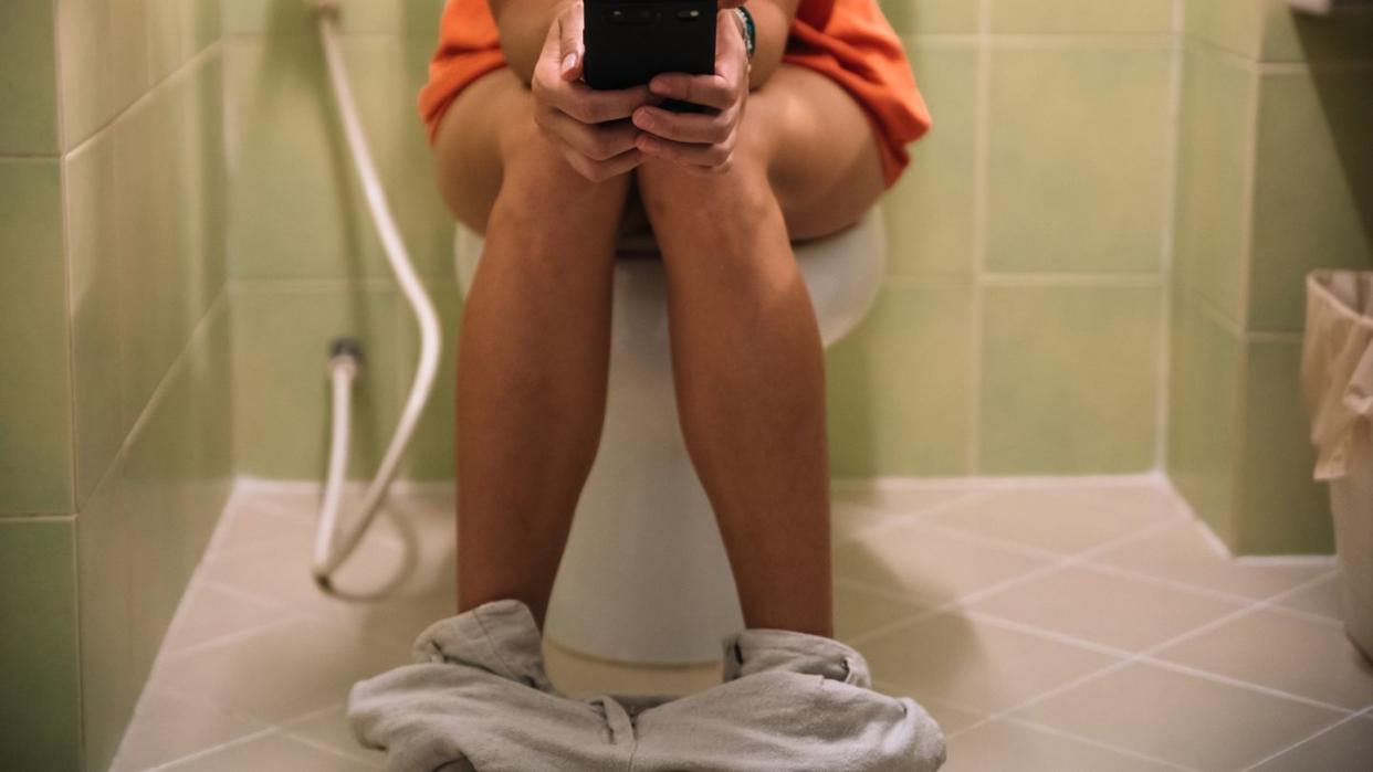 woman sitting on a toilet holding a mobile phone in her hands