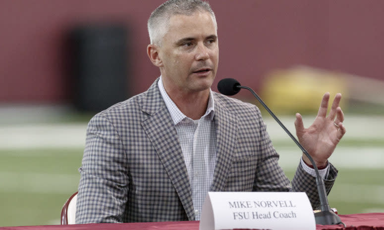 Florida State head coach Mike Norvell addresses a crowd while sitting at a microphone.