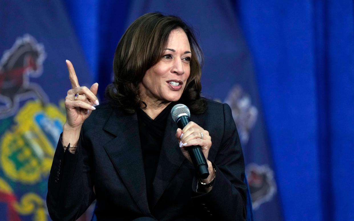 Ms Harris wears black, holds a microphone and gestures with an index finger