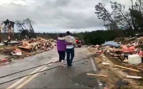 People walk amid debris in Lee County, Ala., after what appeared to be a tornado struck in the area  - Credit: AP