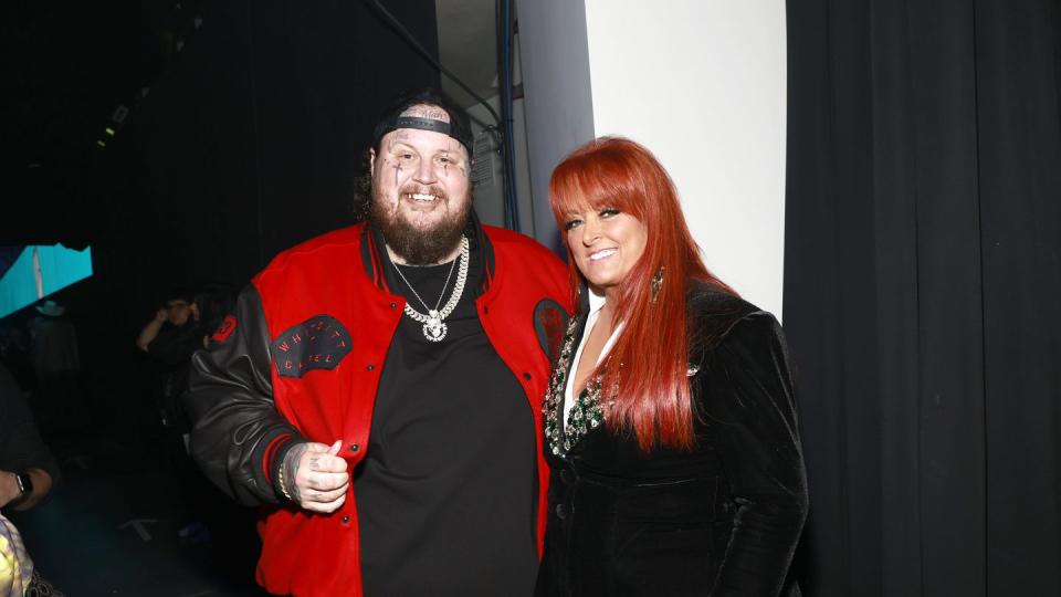 jelly roll and wynonna judd smiling and embracing backstage at an award show