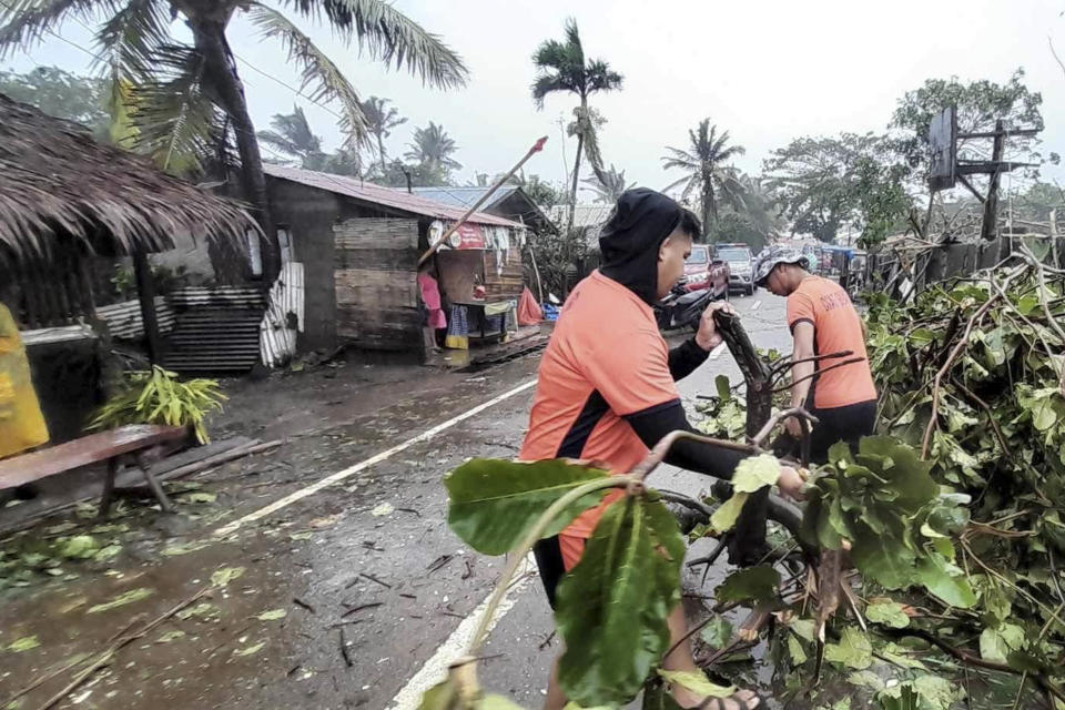 In this photo provided by the Philippine Coast Guard, Coast Guard personnel clear toppled trees caused by Typhoon Doksuri along a road in Claveria, Cagayan province, northern Philippines on Wednesday July 26, 2023. Typhoon Doksuri ripped off tin roofs from homes, engulfed low-lying villages in flood, knocked down power and displaced more than 12,000 people Wednesday as it smashed into a small island and lashed northern Philippine provinces overnight with ferocious wind and rain, officials said. (Philippine Coast Guard via AP)