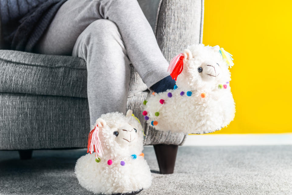 Young girl is wearing cute soft 3d llama slippers, standing on the gray flooring with yellow wall background, trendy colors of 2021