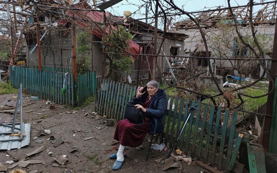A local woman speaks on her phone as she sits on a bench next to a residential house damaged by a Russian missile strike in Mykolaiv - STRINGER/REUTERS
