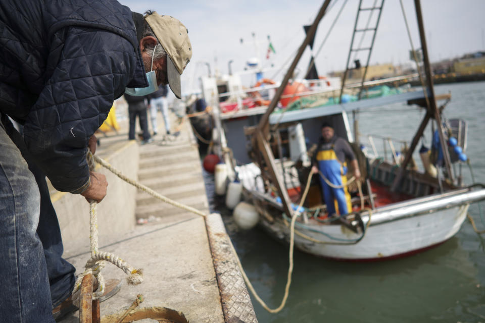 A man, wearing a protective mask, helps docking a fishing boat as it entered Fiumicino fishing port, in the outskirts of Rome Monday, March 30, 2020. Italy’s fishermen still go out to sea at night, but not as frequently in recent weeks since demand is down amid the country's devastating coronavirus outbreak. (AP Photo/Andrew Medichini)