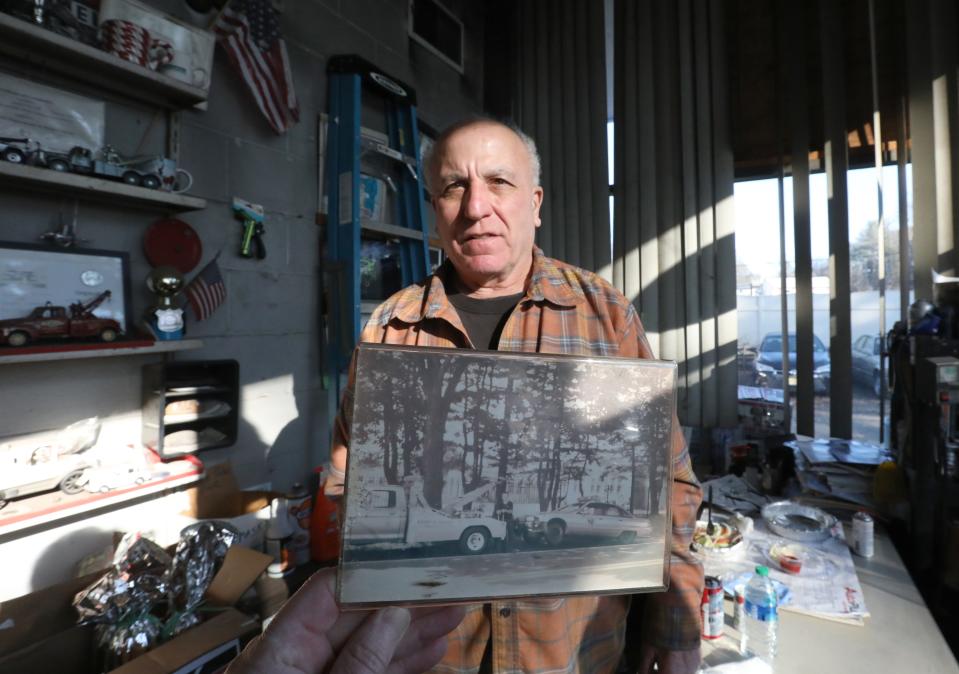 Randy Johnson, owner of Randy's Convent Road Garage in Blauvelt, holds a photo Jan. 5 that he displays in his office. The photo shows his tow truck with the police car he towed to his shop in 1993. The car was damaged while pursuing bank robbers who fired multiple rounds at the police, including a chase through the grounds of Pearl River High School.