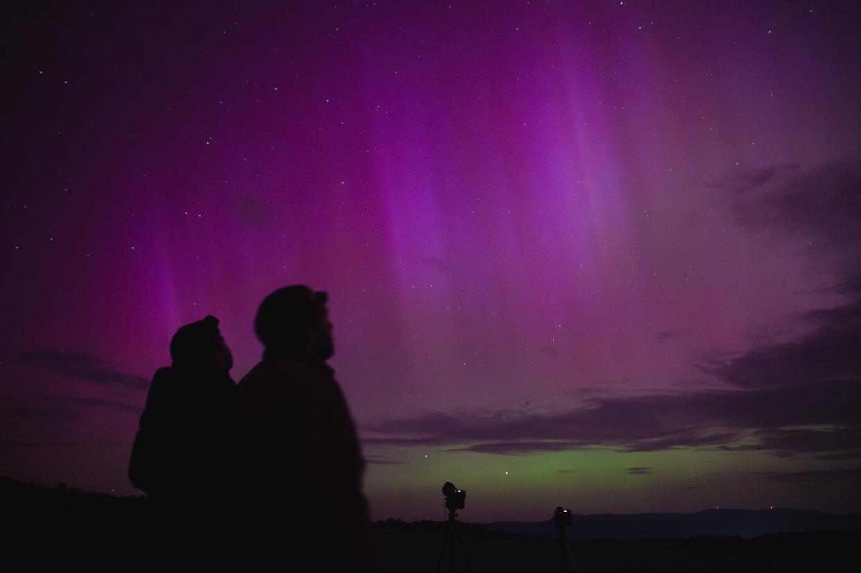  The silohettes of two people on a dazzling purple and green sky filled with auroras. 
