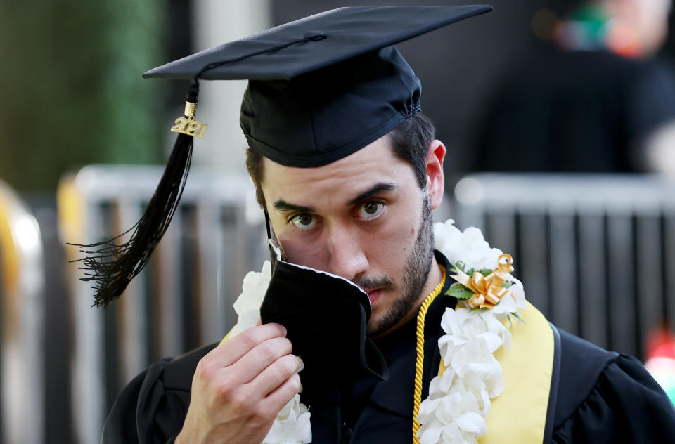 A Cal State Los Angeles graduate wearing a graduation cap removes his face mask