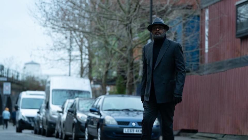 Nick Fury stands on a street in london wearing an all black suit and a hat in secret invasion tv show