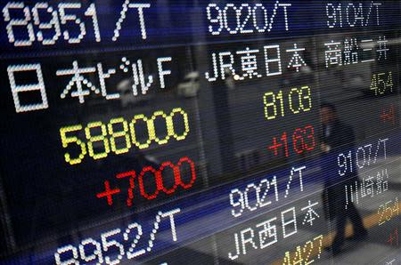 A pedestrian is reflected in an electronic board showing stock prices outside a brokerage in Tokyo January 15, 2014. REUTERS/Yuya Shino