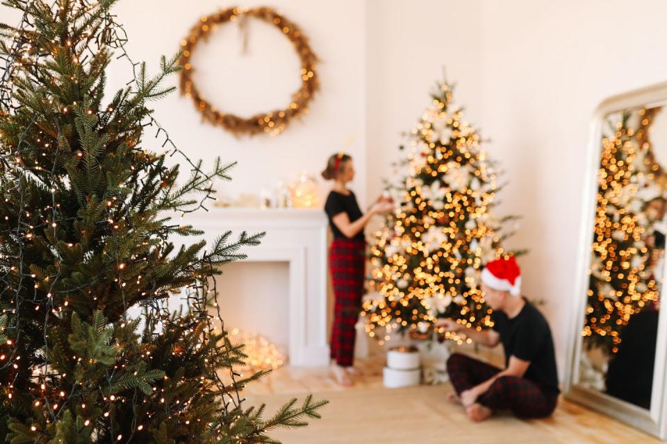 a happy couple in love in pajamas are preparing for the holiday, celebrating christmas and new year by decorating a christmas tree in the cozy interior of the house in winter in december