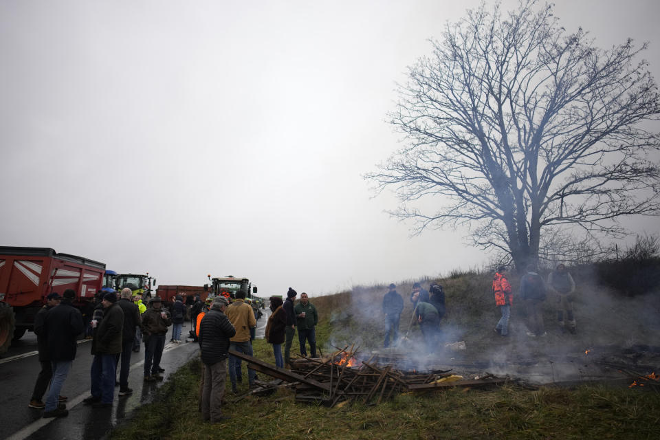 Farmers rest at a bonfire a they block a highway leading to Paris, Friday, Jan. 26, 2024 in Saclay, south of Paris. Snowballing protests by French farmers crept closer to Paris with tractors driving in convoys and blocking roads in many regions of the country to ratchet up pressure for government measures to protect the influential agricultural sector from foreign competition, red tape, rising costs and poverty-levels of pay for the worst-off producers. (AP Photo/Christophe Ena)