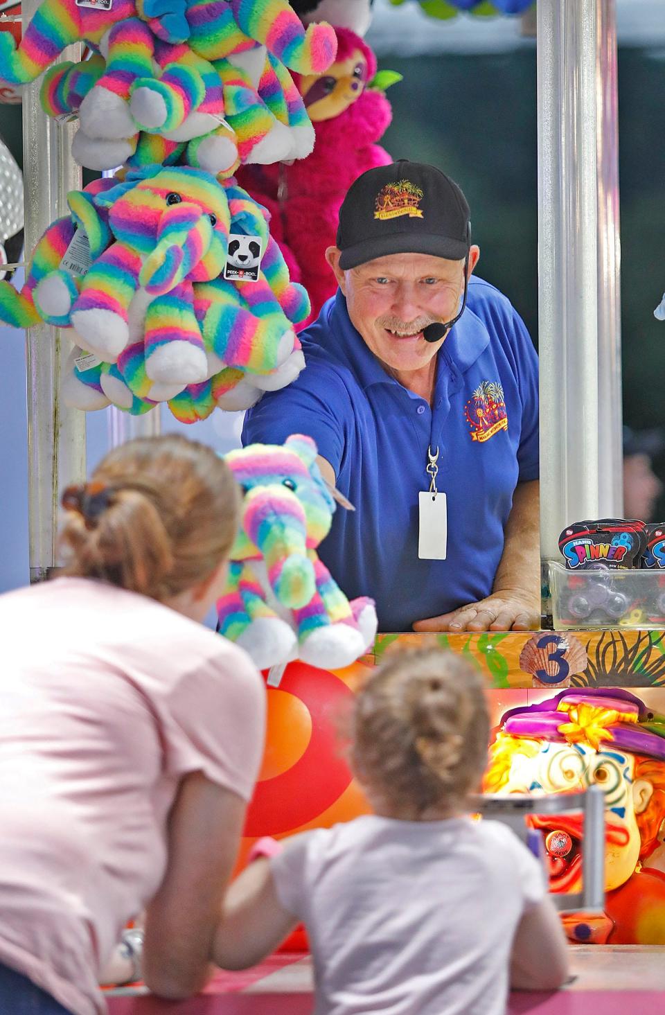 Marshfield Fair carny Larry Creed asks a mother what prize her daughter would like for winning. She selected the rainbow-colored stuffed elephant. Monday, Aug. 21 2023.