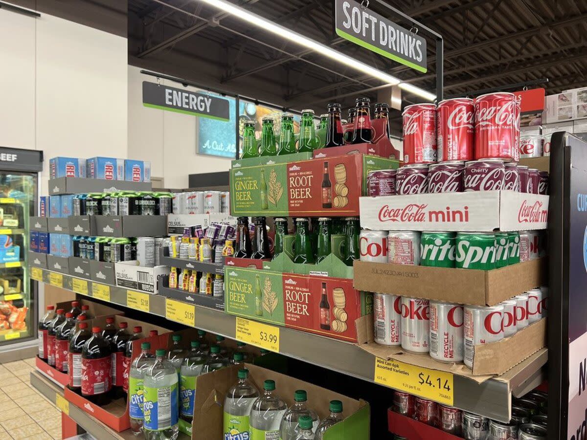 Soft drinks section at Aldi, Knoxville, Tennessee, several cardboard boxes piled upon each other, refrigerated section in the background