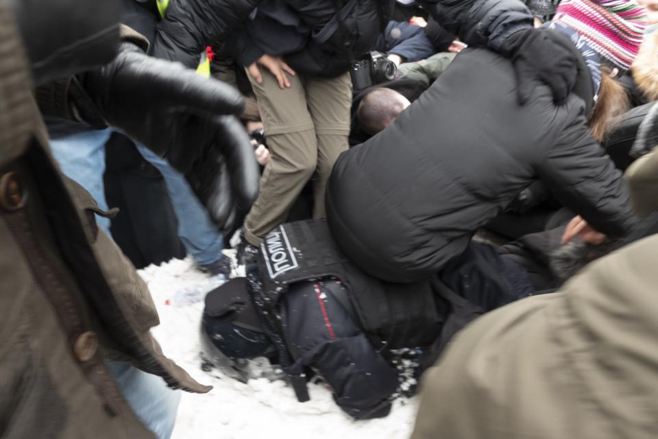 Demonstrators sit on a policeman lying in the snow during a protest against the jailing of opposition leader Alexei Navalny in Pushkin square in Moscow, Russia, Saturday, Jan. 23, 2021. Russian police arrested more than 3,400 people Saturday in nationwide protests demanding the release of opposition leader Alexei Navalny, the Kremlin's most prominent foe, according to a group that counts political detentions. In Moscow, an estimated 15,000 demonstrators gathered in and around Pushkin Square in the city center, where clashes with police broke out and demonstrators were roughly dragged off by helmeted riot officers to police buses and detention trucks. Some were beaten with batons. (AP Photo/Viktor Berezkin)