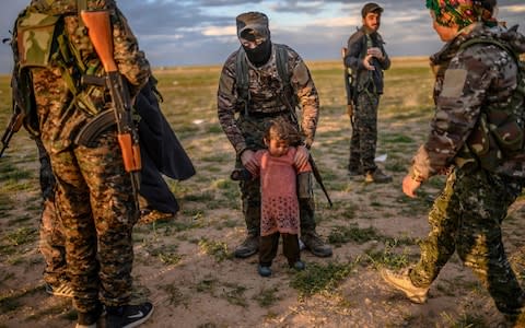 A member of the SDF holds a toddler during a security check of her and her mother (unseen) after they left Isil's last holdout of Baghuz - Credit: AFP