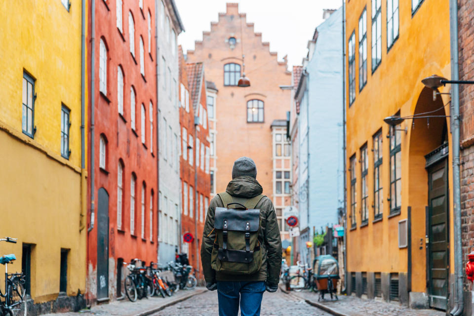 Person with backpack standing in cobblestone street between old buildings