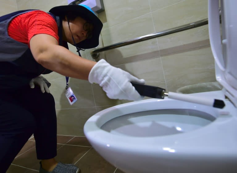 A member of Seoul's 'hidden camera-hunting' squad moves a hand-held detector around the toilet seat of a women's bathroom stall in search of a 'secret camera'