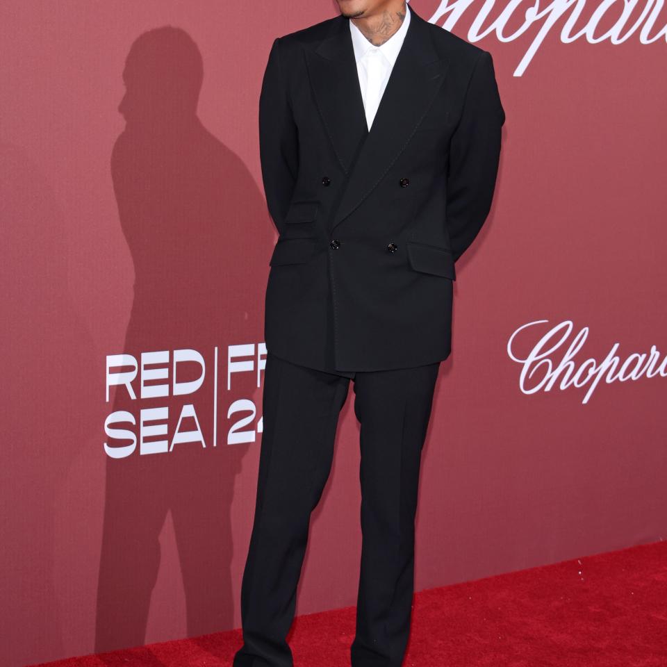 Alexander Edwards in a black suit and white shirt smiling on the red carpet at an event