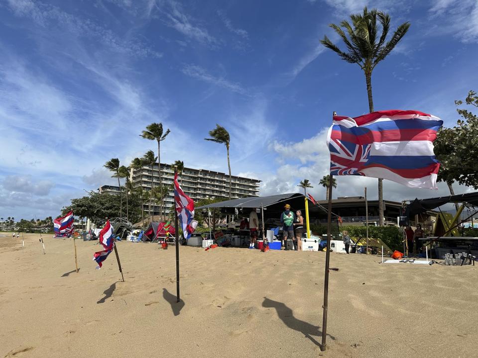 Upside down Hawaiian flags, a sign of distress, blow in the wind at a Fishing for Housing protest in front of resort hotels on Kaanapali Beach in Lahaina, Hawaii on Wednesday, Nov.14, 2023. A group of Lahaina wildfire survivors is vowing to camp on a popular resort beach until the mayor uses his emergency powers to shut down unpermitted vacation rentals and make the properties available for residents in desperate need of housing. (AP Photo/Audrey McAvoy)