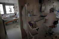 A medical staff checks his computer while a patient affected with the COVID-19 virus lays in a bed in the ICU unit at the Charles Nicolle public hospital, Thursday, April 15, 2021 in Rouen, France. A renewed crush of COVID-19 cases is again forcing intensive care units across France to grapple with the macabre mathematics of how to make space for thousands of critically ill patients (AP Photo/Christophe Ena)