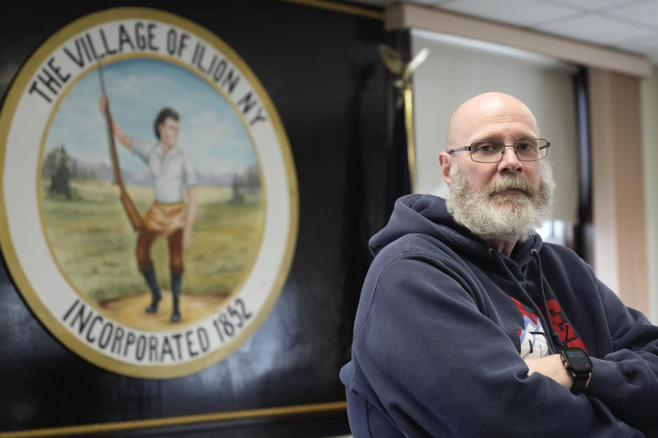 Ilion Mayor John Stephens poses for a picture in front of the seal of the village at the municipal building in Ilion, N.Y., Thursday, Feb. 1, 2024. The seal features Eliphalet Remington, the founder of Remington Arms Co. (AP Photo/Seth Wenig)