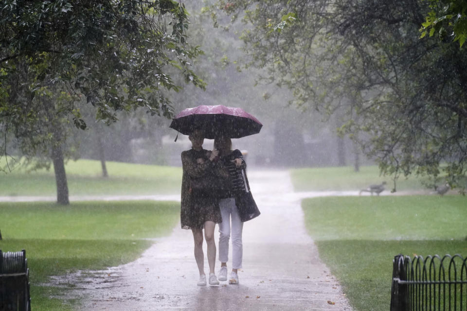 Two women walks through heavy rain in St James's Park in central London, Sunday July 25, 2021. Thunderstorms bringing lightning and torrential rain to the south are set to continue until Monday it is forecast. (Victoria Jones/PA via AP)