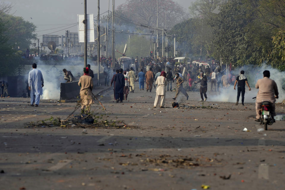 Supporters of former Prime Minister Imran Khan throw stones toward riot police officers firing tear gas to disperse them during clashes, in Lahore, Pakistan, Wednesday, March 15, 2023. Clashes between Pakistan's police and supporters of Khan continued outside his home in the eastern city of Lahore on Wednesday, a day after officers went to arrest him for failing to appear in court on graft charges. (AP Photo/K.M. Chaudary)