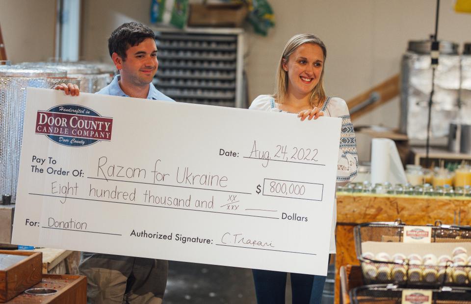 Door County Candle Co. owner Christiana Gorchynsky Trapani, a second-generation Ukrainian, and her husband, Nic, show a check for $800,000 indicating the amount the company has donated through sales of its Ukraine candles and other candles to Razom for Ukraine for emergency relief help during an Aug. 24 ceremony at the Sturgeon Bay shop.