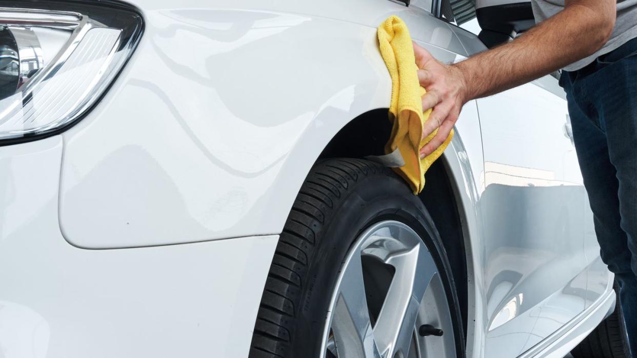 close up view of a worker detailing polishing a white car with a rag