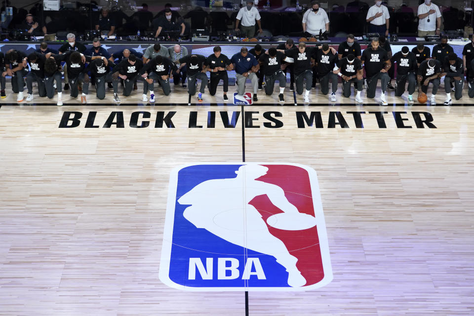 Members of the New Orleans Pelicans and Utah Jazz kneel together around the Black Lives Matter logo on the court during the national anthem before the start of an NBA basketball game Thursday, July 30, 2020, in Lake Buena Vista, Fla. (AP Photo/Ashley Landis, Pool)