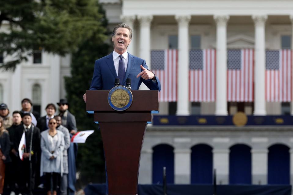 Gov. Gavin Newsom smiles while speaking at a lectern.