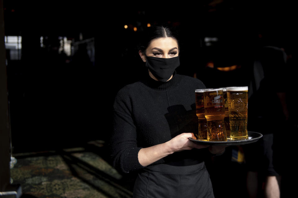 A member of the bar staff carries drinks to outdoor tables at the reopening of the Figure of Eight pub, in Birmingham, England, Monday April 12, 2021. Millions of people in England will get their first chance in months for haircuts, casual shopping and restaurant meals on Monday, as the government takes the next step on its lockdown-lifting road map. (Jacob King/PA via AP)