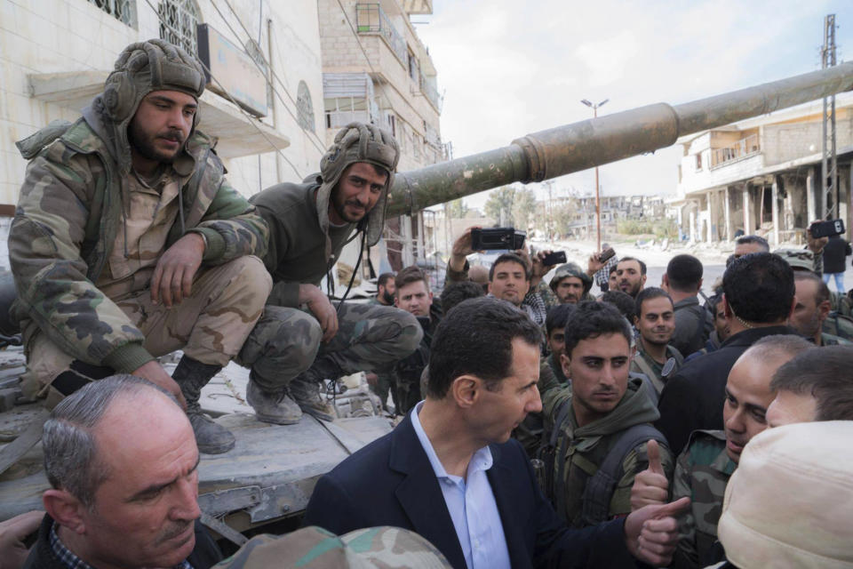 FILE - In this March 18, 2018, file photo released on the official Facebook page of the Syrian Presidency, Syrian President Bashar Assad, center, speaks with Syrian troops during his visit to the front line in the newly captured areas of eastern Ghouta, near the capital Damascus, Syria. Assad has snapped up a prize from world powers that have been maneuvering in his country’s multifront wars. Without firing a shot, his forces are returning to towns and villages in northeastern Syria where they haven’t set foot for years. (Syrian Presidency Facebook Page via AP, File)