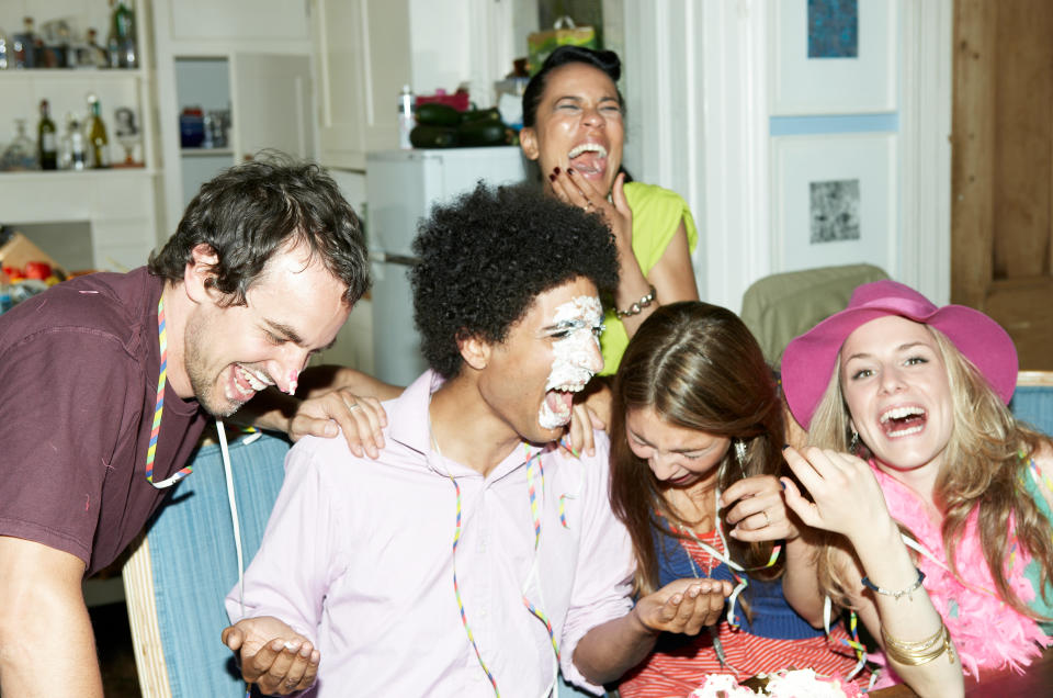 A group of people laughing together at a party, one with a face covered in cake