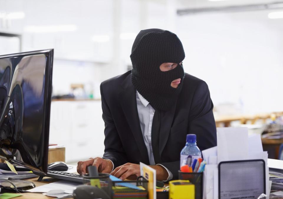 A person types on a keyboard while wearing a ski mask.