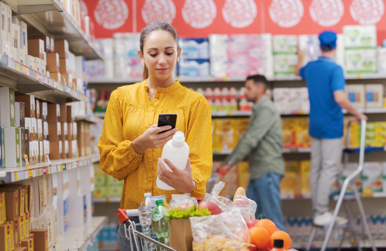 Woman buying groceries at the supermarket, she is checking products information using a scanner app on her smartphone