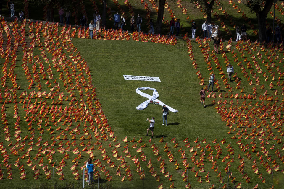 People walk among the Spanish flags placed in memory of coronavirus (COVID-19) victims in Madrid, Spain, Sunday, Sept. 27, 2020. An association of families of coronavirus victims has planted what it says are 53,000 small Spanish flags in a Madrid park to honor the dead of the pandemic. (AP Photo/Manu Fernandez)